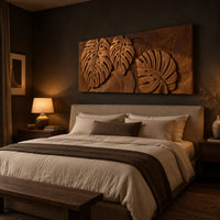 Wood wall art with three carved split leaves in deep relief above a bed in a dusk lit bedroom