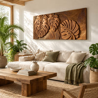 Wood wall art with three carved split leaves in deep relief in a bright sunroom with green plants