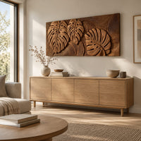 Wood wall art with three carved split leaves in deep relief above a light oak sideboard in daylight