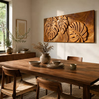 Wood wall art with three carved split leaves in deep relief beside a dining table in natural light