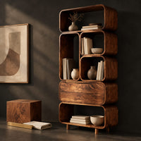 Corner detail of tall stacked bookshelf of soft edged cubbies with a wide drawer beside wood, brass and linen samples