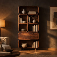 Tall stacked bookshelf of soft edged cubbies with a wide drawer in a dark living room at golden hour