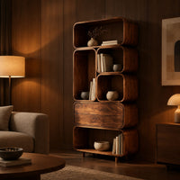 Tall stacked bookshelf of soft edged cubbies with a wide drawer in an evening living room with walnut wall paneling