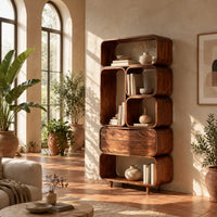 Tall stacked bookshelf of soft edged cubbies with a wide drawer in a bright living room with arched windows and plants