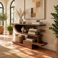 Open shelf console table with staggered shelves on a stepped base in a bright entryway with arched windows and plants