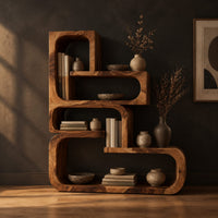 Stepped bookshelf of chunky open cubbies with offset shelves in a dark studio against a charcoal plaster wall