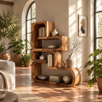 Stepped bookshelf of chunky open cubbies with offset shelves in a bright living room with arched windows and plants