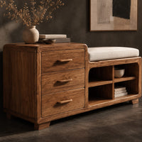 Corner detail of low wooden bench with three drawers, four open cubbies and a cushioned seat beside wood, brass and linen samples