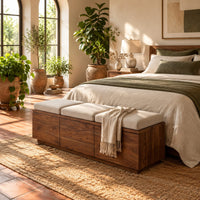 Low wooden bench with three seat cushions and a three panel front in a bright bedroom with arched windows and plants