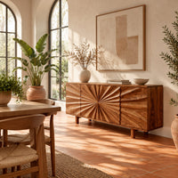 Sideboard with a sunburst carved center panel and short legs in a bright dining room with arched windows and plants