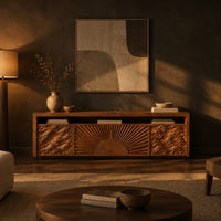Tv stand with a carved sunburst center and wave relief side panels in a dark living room at golden hour