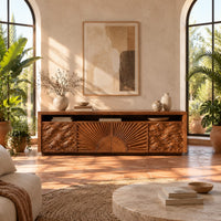 Tv stand with a carved sunburst center and wave relief side panels in a bright living room with arched windows and plants