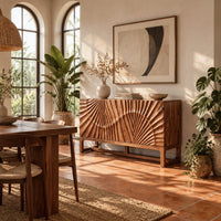 Sideboard with sunburst carving across the front on a slim open frame base in a bright dining room with arched windows and plants