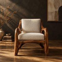 Wooden armchair with sweeping looped arms and soft cream cushions in a dark studio against a charcoal plaster wall