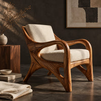 Corner detail of wooden armchair with sweeping looped arms and soft cream cushions beside wood, brass and linen samples