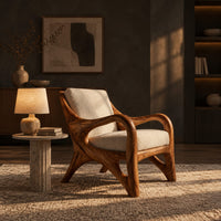 Wooden armchair with sweeping looped arms and soft cream cushions in a dark living room at golden hour