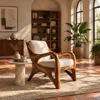 Wooden armchair with sweeping looped arms and soft cream cushions in a bright living room with arched windows and plants