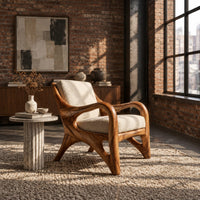 Wooden armchair with sweeping looped arms and soft cream cushions in an industrial loft living room with exposed brick