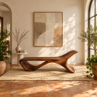 Low sweeping bench with an open loop underside and a raised end in a bright entryway with arched windows and plants