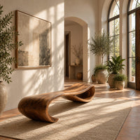 Long wooden bench shaped like a ribbon with a rolled end in a bright entryway with arched windows and plants