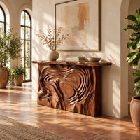 Console table with a swirl carved front and a thick natural edge top in a bright entryway with arched windows and plants