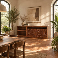 Sideboard with two swirl carved doors and open shelf bays at one end in a bright dining room with arched windows and plants