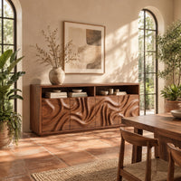 Wood sideboard with swirl carved front panels and two open shelves along the top in a bright dining room with arched windows and plants