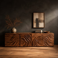 Low wooden tv stand with swirl carved front panels in a dark studio against a charcoal plaster wall