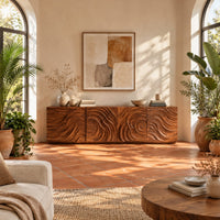 Low wooden tv stand with swirl carved front panels in a bright living room with arched windows and plants