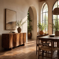 Wavy front sideboard with four panels of swirling wood grain in a bright dining room with arched windows and plants