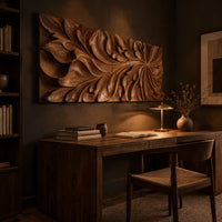 Wide wooden relief panel carved with swirling overlapping leaves above a desk in a dark study corner