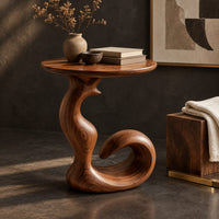 Corner detail of round side table on a swirling pedestal with a curled foot beside wood, brass and linen samples