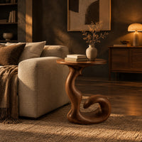 Round side table on a swirling pedestal with a curled foot in a dark living room at golden hour