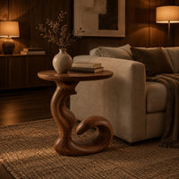 Round side table on a swirling pedestal with a curled foot in an evening living room with walnut wall paneling