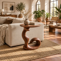 Round side table on a swirling pedestal with a curled foot in a bright living room with arched windows and plants