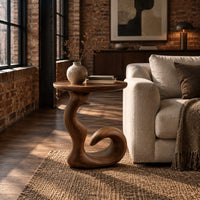 Round side table on a swirling pedestal with a curled foot in an industrial loft living room with exposed brick