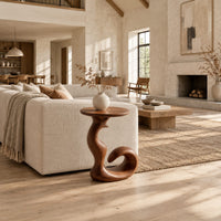 Round side table on a swirling pedestal with a curled foot in a bright open plan living room