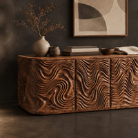 Corner detail of long sideboard with four doors carved in deep swirling ripples beside wood, brass and linen samples