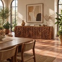 Long sideboard with four doors carved in deep swirling ripples in a bright dining room with arched windows and plants