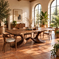 Dining table with a soft edged top on a swooping wave base in a bright dining room with arched windows and plants