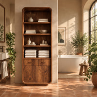 Tall bathroom cabinet with four open shelves above two small drawers and two doors in a bright bathroom with arched windows and plants