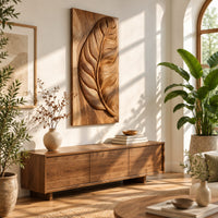 Tall wood panel carved in deep relief with one large leaf and fine veins in a bright sunroom with green plants