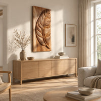 Tall wood panel carved in deep relief with one large leaf and fine veins above a light oak sideboard in daylight