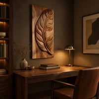 Tall wood panel carved in deep relief with one large leaf and fine veins above a desk in a dark study corner