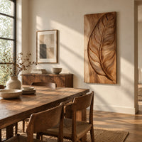 Tall wood panel carved in deep relief with one large leaf and fine veins beside a dining table in natural light