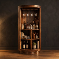 Tall cylinder bar cabinet with a glass rail on top and open cubbies below in a dark studio against a charcoal plaster wall