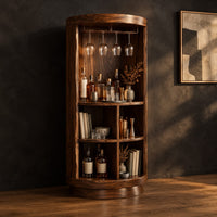 Tall cylinder bar cabinet with a glass rail on top and open cubbies below, three-quarter view showing the grain