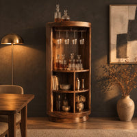 Tall cylinder bar cabinet with a glass rail on top and open cubbies below in a dark dining room at golden hour