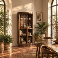 Tall cylinder bar cabinet with a glass rail on top and open cubbies below in a bright dining room with arched windows and plants