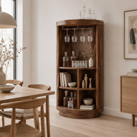 Tall cylinder bar cabinet with a glass rail on top and open cubbies below in a Scandinavian dining room with white walls